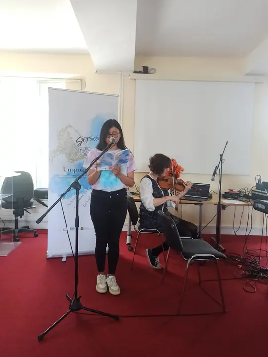 A young writer reading at the microphone beside a violinist