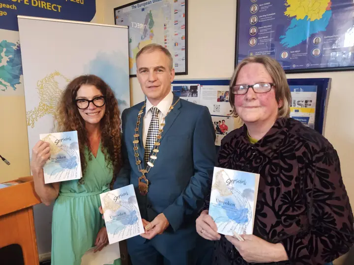 Three people holding copies of Unspoken in front of the SiarScéal banner